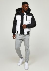 Puffer jacket with a black and white color block design, featuring a faux fur-lined hood, zippered pocket, and elastic cuffs; paired with gray sweatpants.