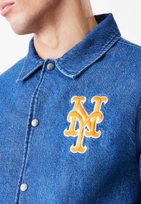 Modrá džínová bunda s límečkem a zapínáním na patentky. Na prsou má oranžovou vyšívanou položku "NY". Hladký povrch.
