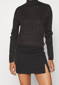 Schwarzer gerippter Rollkragenpullover mit langen Ärmeln, kombiniert mit einem schwarzen Minirock mit seitlichem Schlitz. Glatte Textur und figurbetontes Design.