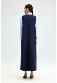 Robe sans manches bleu marine avec une silhouette droite, associée à une chemise collée bleu clair en dessous, présentant un design épuré et minimaliste.