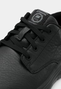 Chaussure de travail Skechers en cuir noir avec lacets noirs et étiquette « Skechers Authentic Work » sur la languette rembourrée.