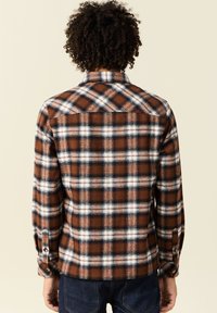 Camicia di flanella a quadri marrone e bianco con polsini abbottonati, caratterizzata da un colletto classico e un design a yoke sulla schiena. Texture morbida e calda.