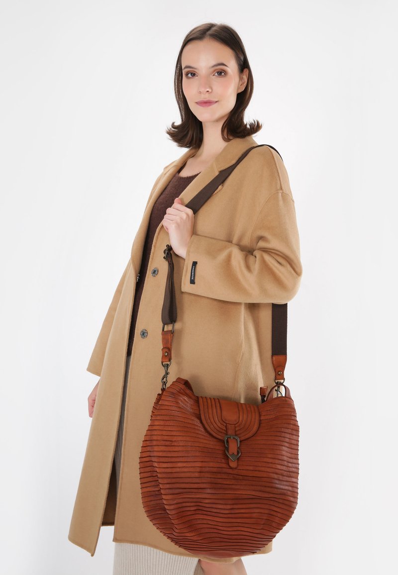Sac à épaule en cuir brun avec une texture côtelée, une forme incurvée et une sangle ajustable, doté d'une fermeture à cliquet en métal.