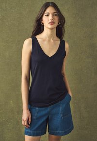 Marineblå ærmeløs top med V-udskæring, parret med lyseblå denimshorts med sidelommer og opbrydede kanter.
