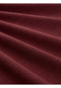 Burgunderroter Stoff mit weicher Textur, der wellenförmige Falten und eine glatte Oberfläche aufweist und im Licht einen leichten Glanz betont.