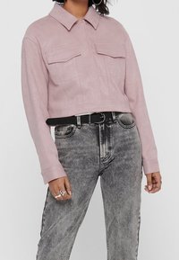 Avskuren rosa mockajacka med krage, två bröstfickor och slät yta, tillsammans med högmidjade svarta och grå denimjeans.
