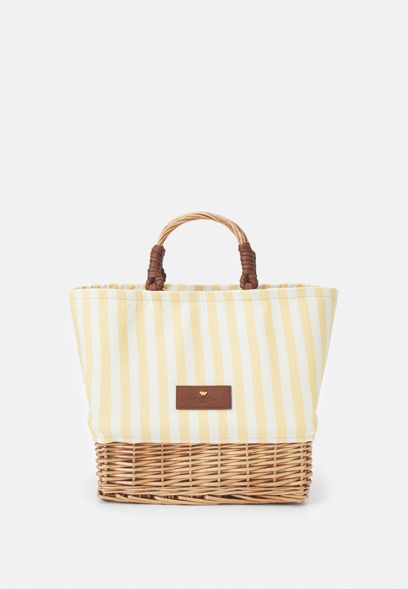 Sac fourre-tout rayé jaune et blanc avec un fond en osier tressé, des accents en cuir marron et une poignée tressée. Design simple et fonctionnel.