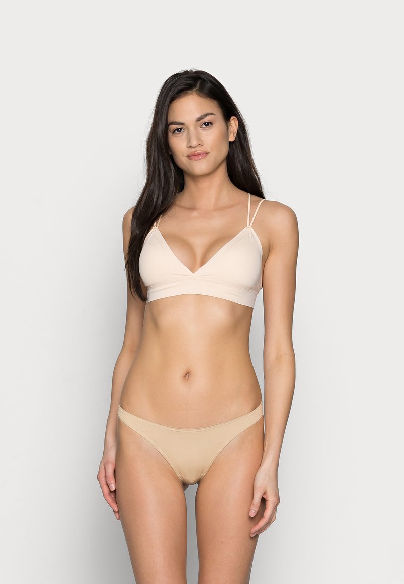 Bralette couleur chair avec un design en V et des bretelles fines. Culottes hipster assorties avec une texture lisse et des coutures minimales.
