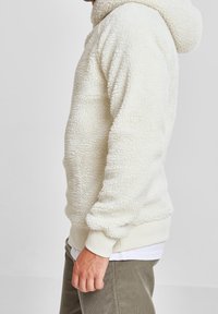 Cremefarvet fleece-hoodie med en tekstureret, fluffy overflade. Den har en front kangaroo-lomme og ribbede manchetter og kant.