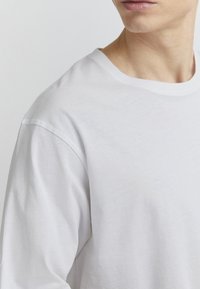 White cotton t-shirt with a classic crew neckline, short sleeves, and soft texture, showing a close-up of the shoulder and collar area.