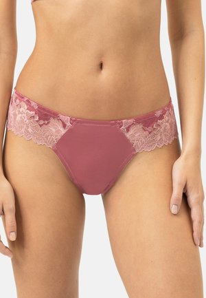Femme portant un bikini mauve bordé de dentelle, visible de la taille aux cuisses supérieures sur un fond uni.