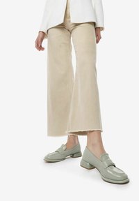 Groene patenten leren instappers met een ronde neus, een decoratieve band en een lage blokhak, gedragen met brede beige cropped broeken.