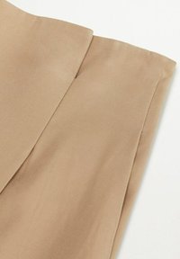 Zbliżenie beżowego materiału z zagiętym brzegiem i widoczną teksturą splotu na białym tle.