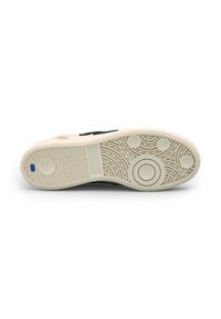 Sole di sneaker in gomma beige con motivi di grip testurizzati e un elemento di design circolare. Accenti verde scuro. Forma pulita e minimalista.