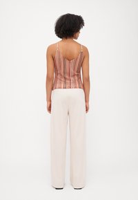 Topi tanpa lengan dengan garis vertikal dalam warna hangat, menampilkan desain punggung berbentuk V. Dipasangkan dengan celana pants lebar berwarna krim yang mengalir.