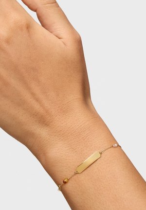 Wrist with a delicate gold chain bracelet featuring a small rectangular gold plate and three tiny beads in yellow, red, and pink.