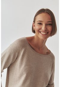 Beige Pullover mit langen Ärmeln, rundem Ausschnitt und Raglanärmeln. Weiche Stricktextur mit sichtbaren Nähten.