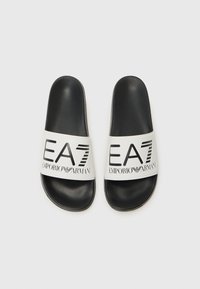 Svarte badesandaler med en hvit rem som har logoen "EA7 EMPORIO ARMANI" i fet svart tekst. Glatt materiale og flat design.