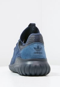 Scarpa sportiva blu con tomaia testurizzata in materiale scamosciato e suola in gomma flessibile. Presenta un design intrecciato e un logo sulla parte posteriore.