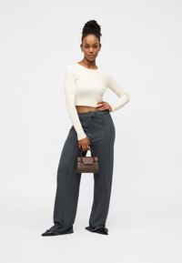 Κρεμ cropped μπλούζα με μακριά μανίκια, φαρδιά γκρι παντελόνια, μαύρα μυτερά παπούτσια και μια μικρή καφέ τσάντα με δομημένο σχέδιο.