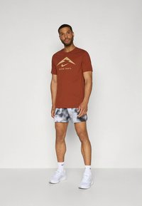 Meeste pruun spordisärk kuldse logoga, hallide lipsuvärvitud lühikestega. Jalatseid kaunistavad valged tossud mustade detailidega.