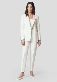 Biały żakiet z pojedynczym guzikem, zestawiony z dopasowanymi spodniami slim fit. Strój wyróżnia się gładką fakturą i minimalistycznym stylem.