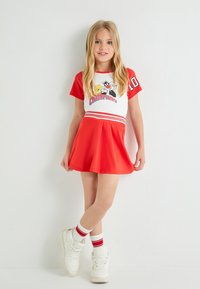Vestido rojo con parte superior blanca con estampado gráfico y mangas rojas, falda plisada, combinado con zapatillas blancas y calcetines a rayas.