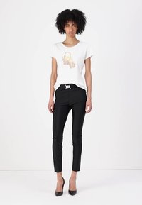 T-shirt bianca con un design grafico di borse; abbinata a pantaloni neri aderenti e tacchi alti; stile minimalista, texture liscia e linee pulite.