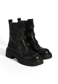 Bottes cheville en cuir noir avec semelles épaisses, ornées de chaînes décoratives et d'un design de bride en zigzag. Texture lisse, style urbain.