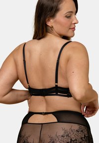 Ensemble de lingerie en dentelle noire comprenant un soutien-gorge structuré avec des bretelles réglables et un bas transparent à motif floral. Fini mat avec des accents dorés.