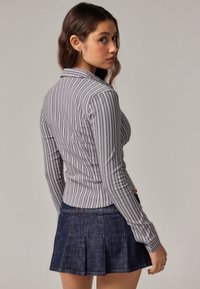 Camisa de rayas gris de manga larga con cuello, combinada con una falda de mezclilla oscura con pliegues. La camisa presenta rayas blancas estrechas.
