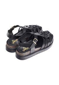 Zwarte geweven sandalen met een stevige bandontwerp, een textuurkurk tussenzool en een platte rubberen zool met een lichte verhoging. Gouden gespdetails waargenomen.