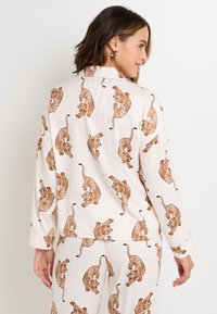 Maglietta da pigiama a maniche lunghe in tessuto morbido, con una stampa beige chiaro di tigri marroni su tutta la superficie. Design con colletto e vestibilità rilassata.