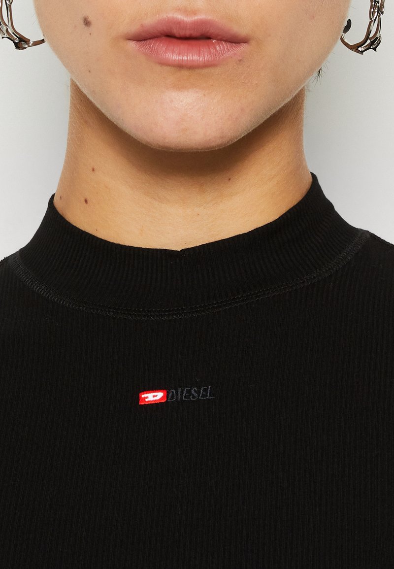 Schwarzes, geripptes Rollkragenoberteil mit einer subtilen Textur, das ein kleines rotes und blaues "DIESEL"-Logo auf der Brust trägt.
