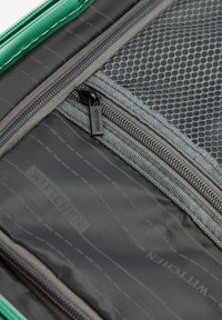 Zelená zipová přihrádka s šedou síťovanou kapsou a vzorovanou textilní podšívkou. Obsahuje značkové zipy a hladký povrch.