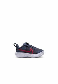 Zapatillas juveniles con parte superior de tejido texturizado en azul oscuro, logotipo rojo de Nike, suela blanca y lengüeta negra en el talón. Diseñadas para la comodidad y el soporte.