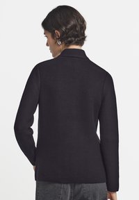 Svart stickad tröja med texturerad yta, långa ärmar och krage, som visar upp en enkel och ren design.