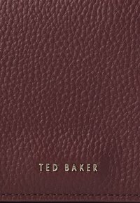 Bordeaux gekleed leren portemonnee met gouden "TED BAKER" logo, met een gerimpelde afwerking en subtiele stikseldetails.