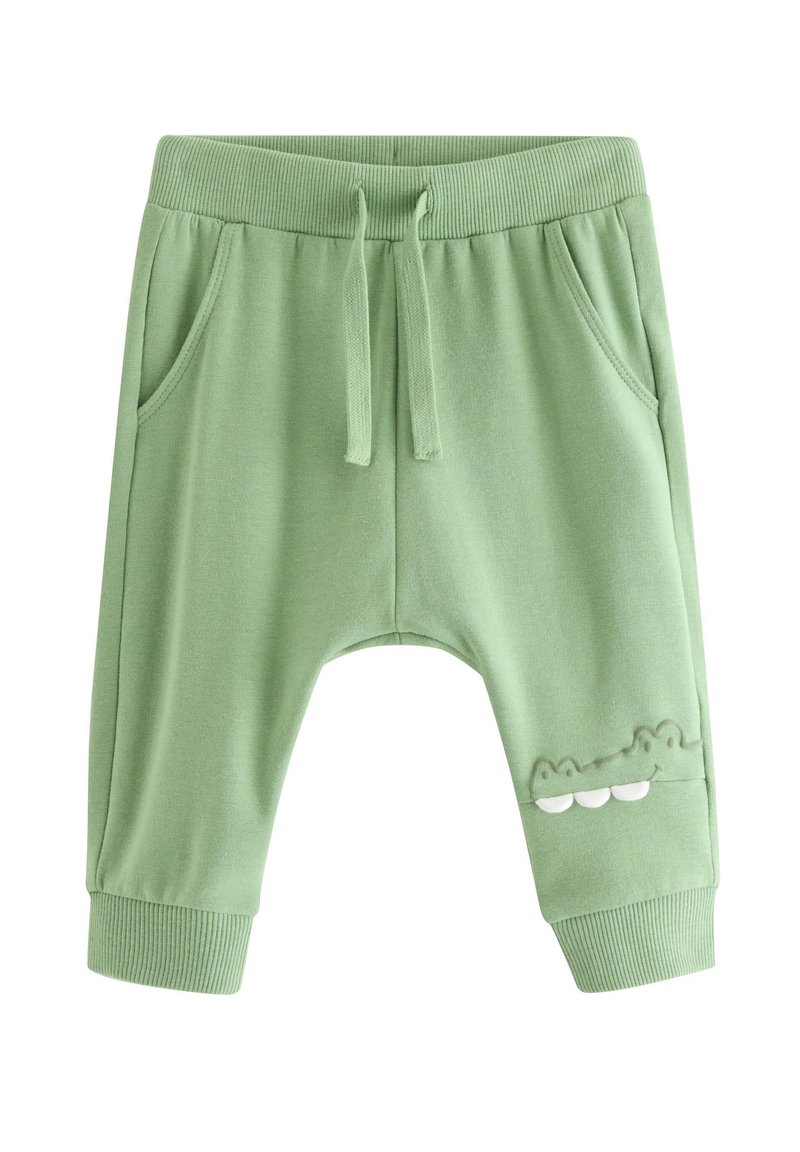Πράσινο βαμβακερό παντελόνι φόρμας με ελαστική μέση, τσέπες και σχέδιο κροκόδειλου με λευκές λεπτομέρειες στο πόδι. Μαλακή υφή, χαλαρή εφαρμογή.
