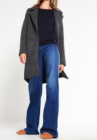 Szary wełniany płaszcz z klapami, z dwiema bocznymi kieszeniami, noszony na granatowej bluzce i niebieskich dzwonowatych dżinsach. Uzupełniają go brązowe buty wsuwane.