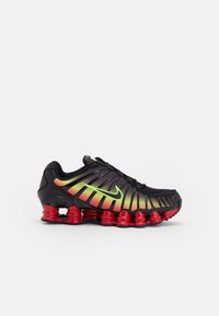 Nike juoksukengät, joissa on musta päällinen, gradienttinen oranssi-keltainen muotoilu ja punainen jousimainen pohja. Ominaisuutena erottuva neonvihreä logo.