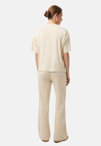 Béžový top s krátkými rukávy a kulatým výstřihem, doplněný o odpovídající rozšířené kalhoty, oba z hladké, měkké látky.
