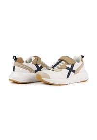 Baskets beiges et blanches avec un design perforé, accents bleu marine, semelle épaisse et lacets. Comprend une sangle velcro pour plus de sécurité.