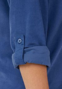 Blaues Baumwollhemd mit gerippter Textur, hochgekrempelten Ärmeln und Knopfdetails. Weicher Stoff mit glatter Oberfläche.