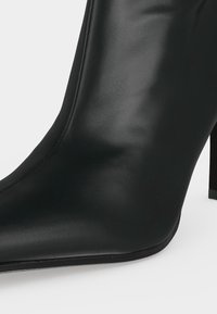 Bottine en cuir noir à bout pointu avec un talon bloc haut et une finition lisse.