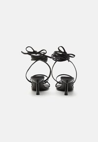 Svarta högklackade sandaler har en elegant design med tunna remmar och dekorativa rosetter vid vristen, vilket framhäver en minimalistsk estetik.
