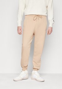 Beiga bomullsjoggers med elastiskt midjeband och dragsko; smal passform med en mjuk textur; parat med vita atletiska sneakers.