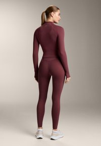 Bordó, hosszú ujjú sportfelső és hozzá illő, rugalmas anyagból készült leggings. A kialakítás testhez simuló sziluettet és magas nyakat kínál.