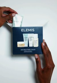 La boîte Elemis Double the Clean présente un design bleu foncé. À l'intérieur se trouvent cinq petits produits de soins de la peau, avec des tubes et un pot, tous étiquetés.