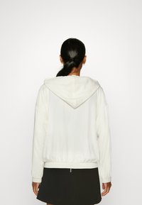 Hvid hoodie med snoretræk i hætten, lange ærmer og ribbede manchetter og kant. Parret med en sort nederdel. Blød tekstur, afslappet pasform.